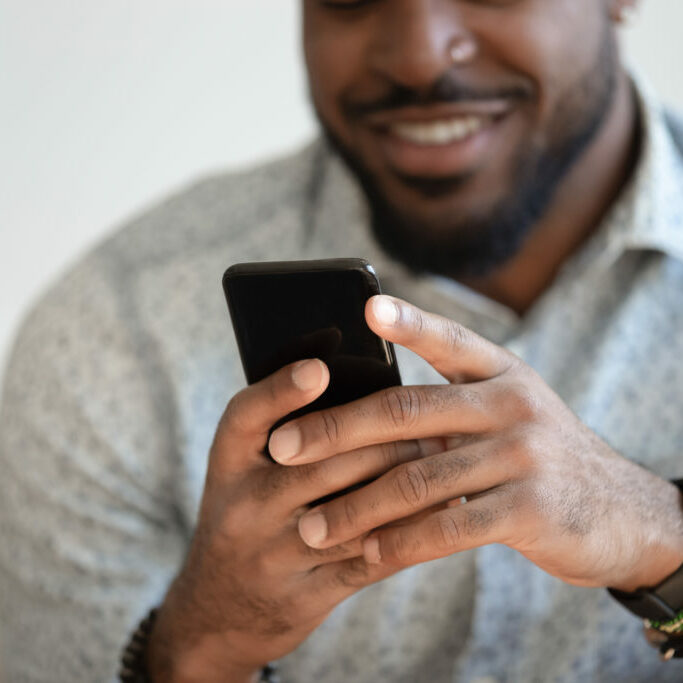 Close up of smiling african American man hold new model modern cellphone texting chatting, happy biracial male use fast connection mobile internet on cellphone browsing web. Technology concept